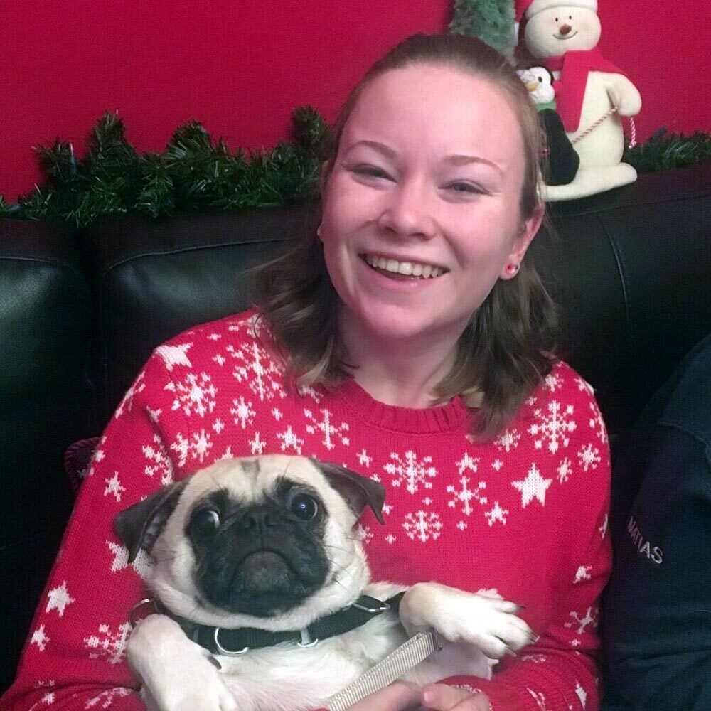 Ariana wearing a Christmas sweater and holding her pug